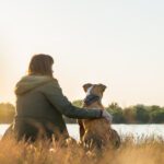 woman sitting by lake with dog